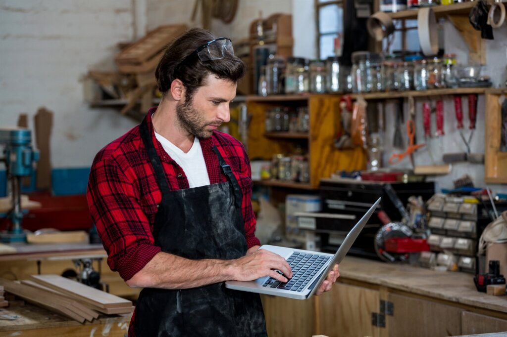 Création site internet artisan : menuisier consultant son site sur un ordinateur portable dans son atelier
